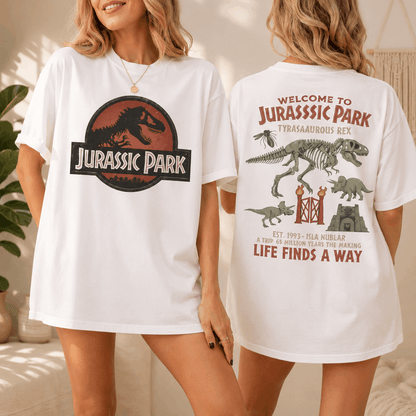 Two women modeling matching oversized white T-shirts with Jurassic Park graphics, showing both the front and back designs in a softly lit indoor setting.