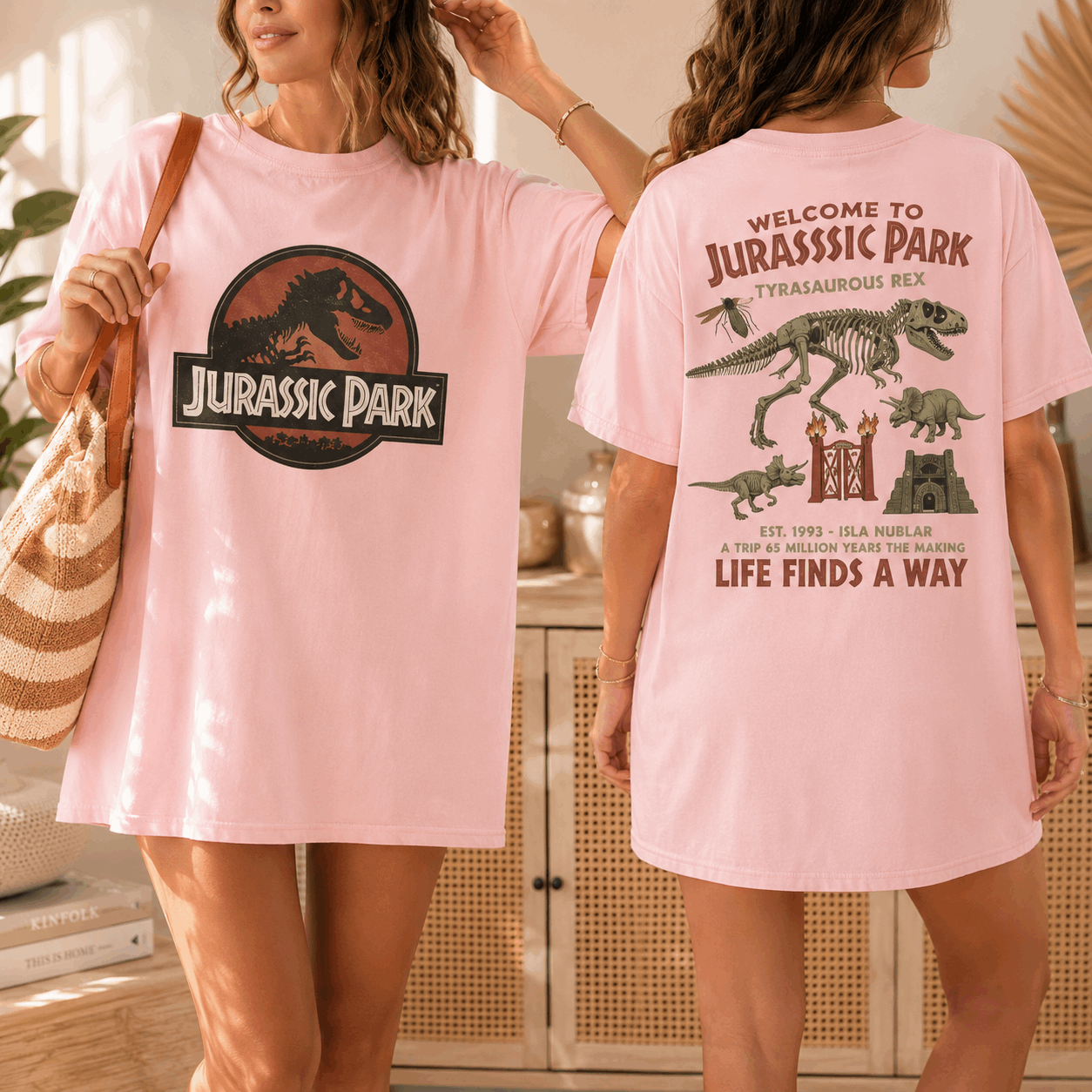 Two women modeling a light pink oversized T-shirt dress in a bright indoor setting, showing both the front and back. The front features a large Jurassic Park logo graphic, and the back has a detailed dinosaur and castle illustration with text.