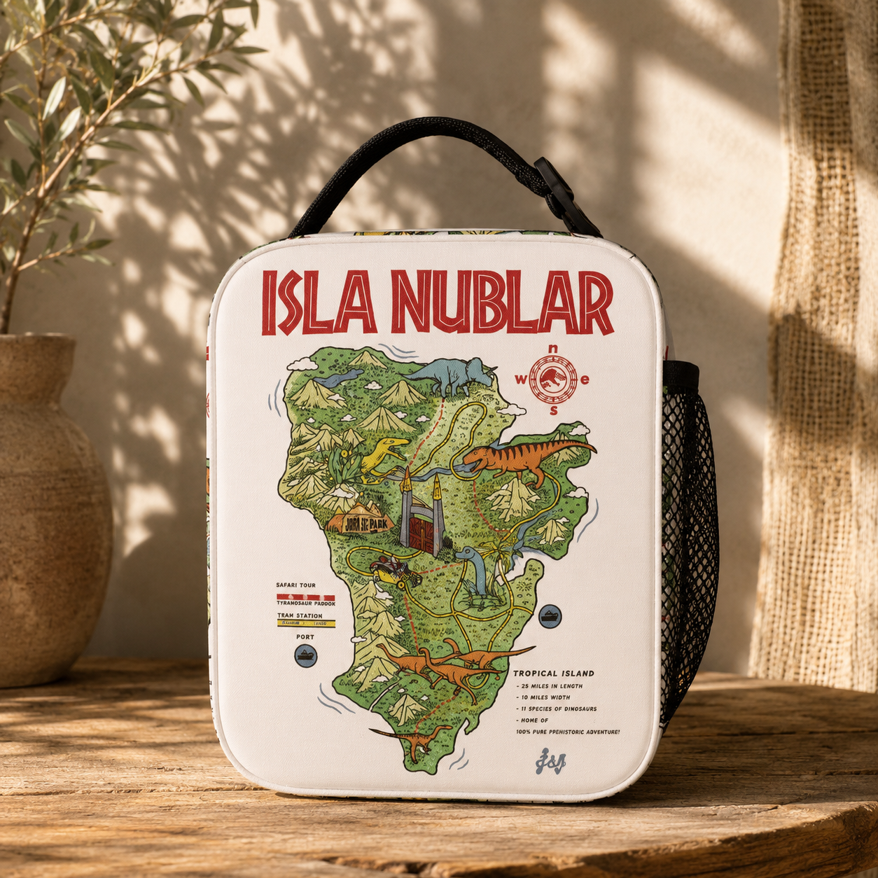 A white insulated lunch bag with a black handle and side pocket, featuring a colorful illustrated map of 'Isla Nublár' on the front, displayed on a rustic wooden surface with a potted plant and burlap in the background.
