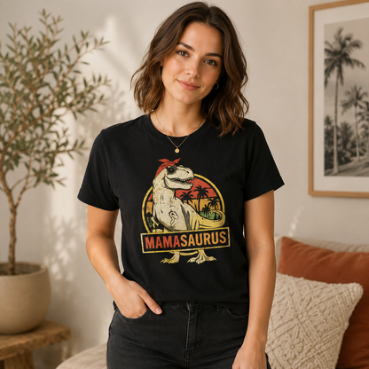 A woman wearing a black graphic t-shirt with a 'MAMASAUROUS' dinosaur design, standing in a cozy room setting with a potted plant and framed picture in the background.