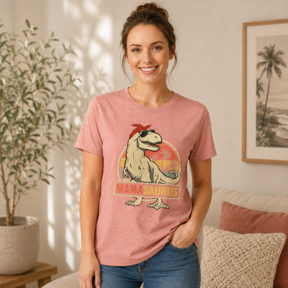 A woman wearing a heathered pink graphic t-shirt with a cartoon Mamasaaurus dinosaur design, standing in a brightly lit living room.