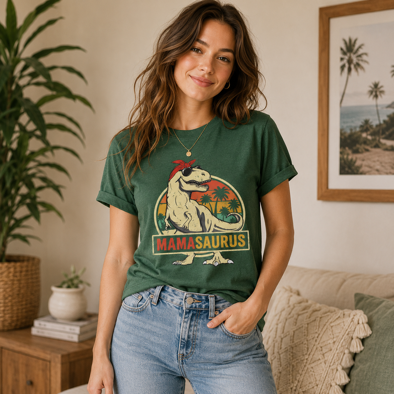 A woman wearing a dark green graphic t-shirt with a retro dinosaur design that reads 'MAMASAUROUS' and 'TODAY', paired with light blue jeans in a cozy living room setting.