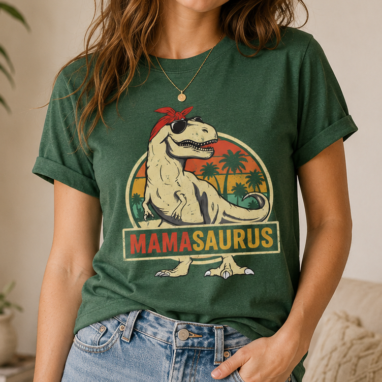 A woman wearing a dark green graphic t-shirt featuring a retro-style 'Mamasaurus' dinosaur design with a red bandana and palm trees, paired with blue jeans.