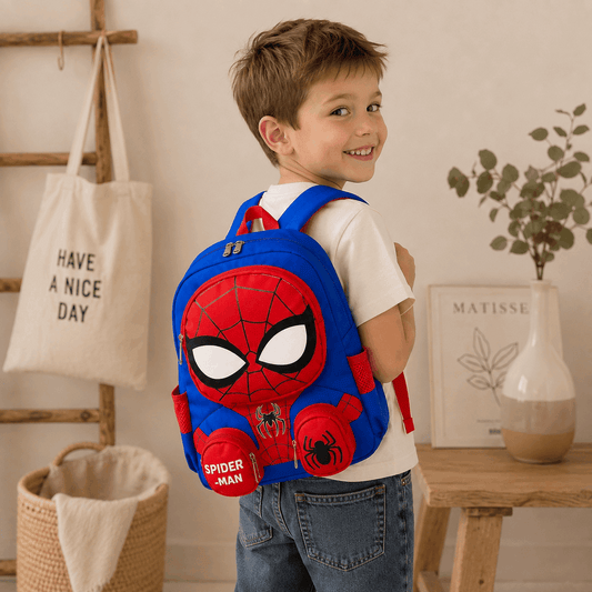 A young boy wearing a white t-shirt and blue jeans is shown from the back, wearing a blue and red Spider-Man themed backpack. The setting is a warm, styled room with a wooden ladder, a canvas tote bag, and a small table with a vase.