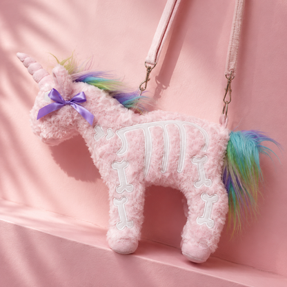 A plush pink unicorn bag with a skeleton bone design on its body, a purple ribbon bow on its neck, and a multicolor pastel mane and tail, shown against a pink background.