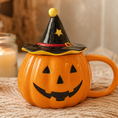 An orange pumpkin-shaped ceramic mug with a carved jack-o'-lantern face, topped with a black witch hat lid featuring a yellow star and red band, set on a textured beige surface with a softly blurred candle in the background.