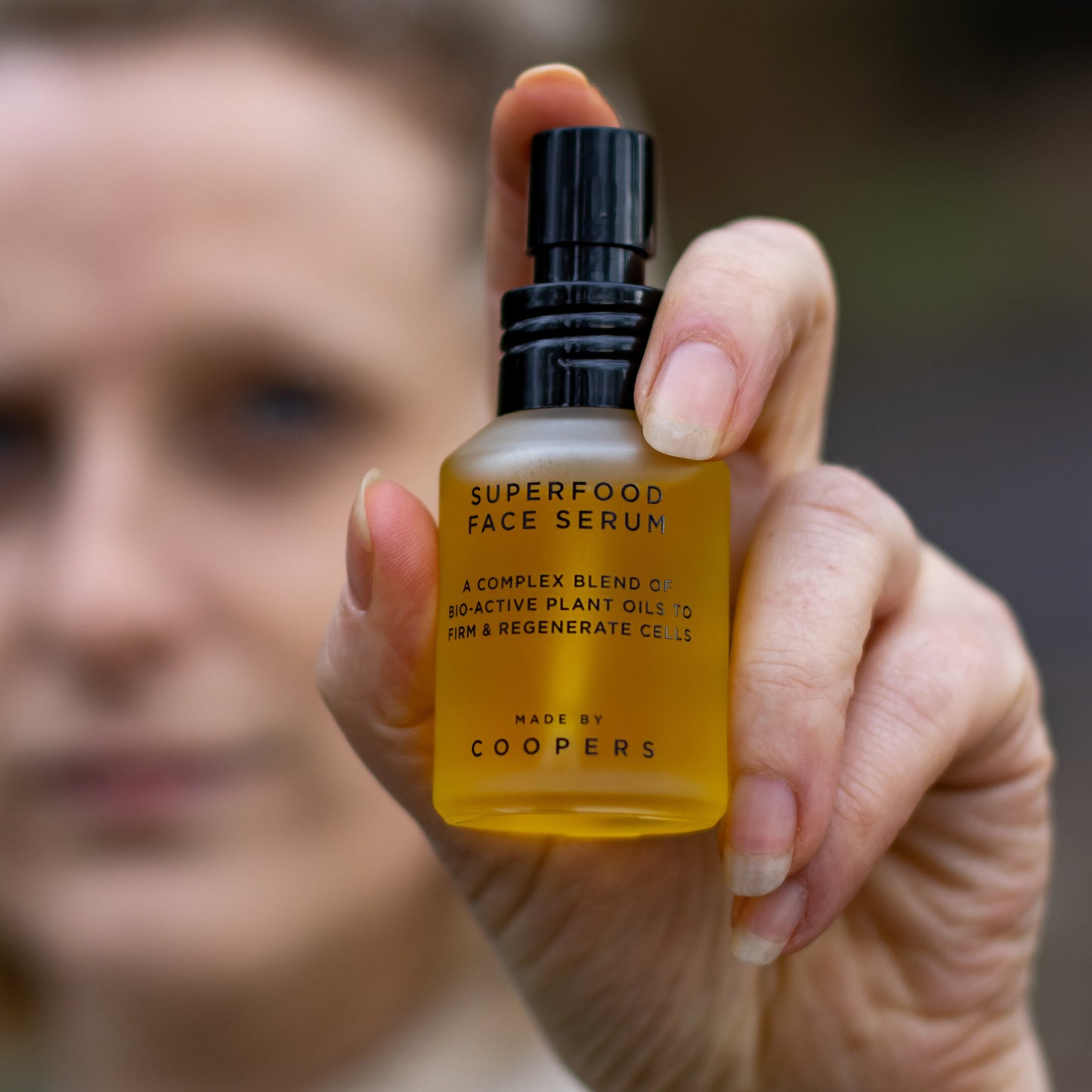 Hand holding a bottle of Superfood Face Serum with a blurred background