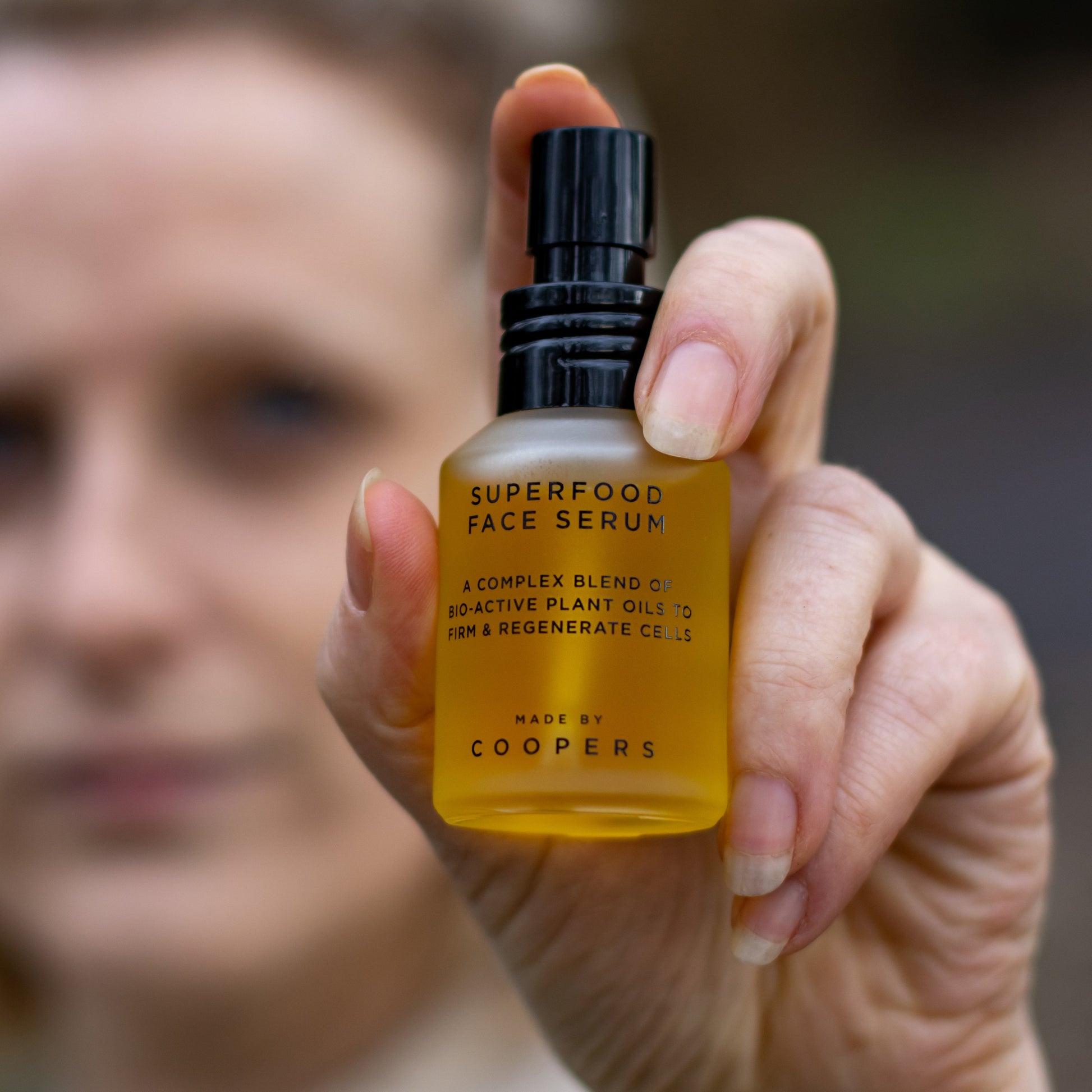 Hand holding a bottle of Superfood Face Serum with a blurred background