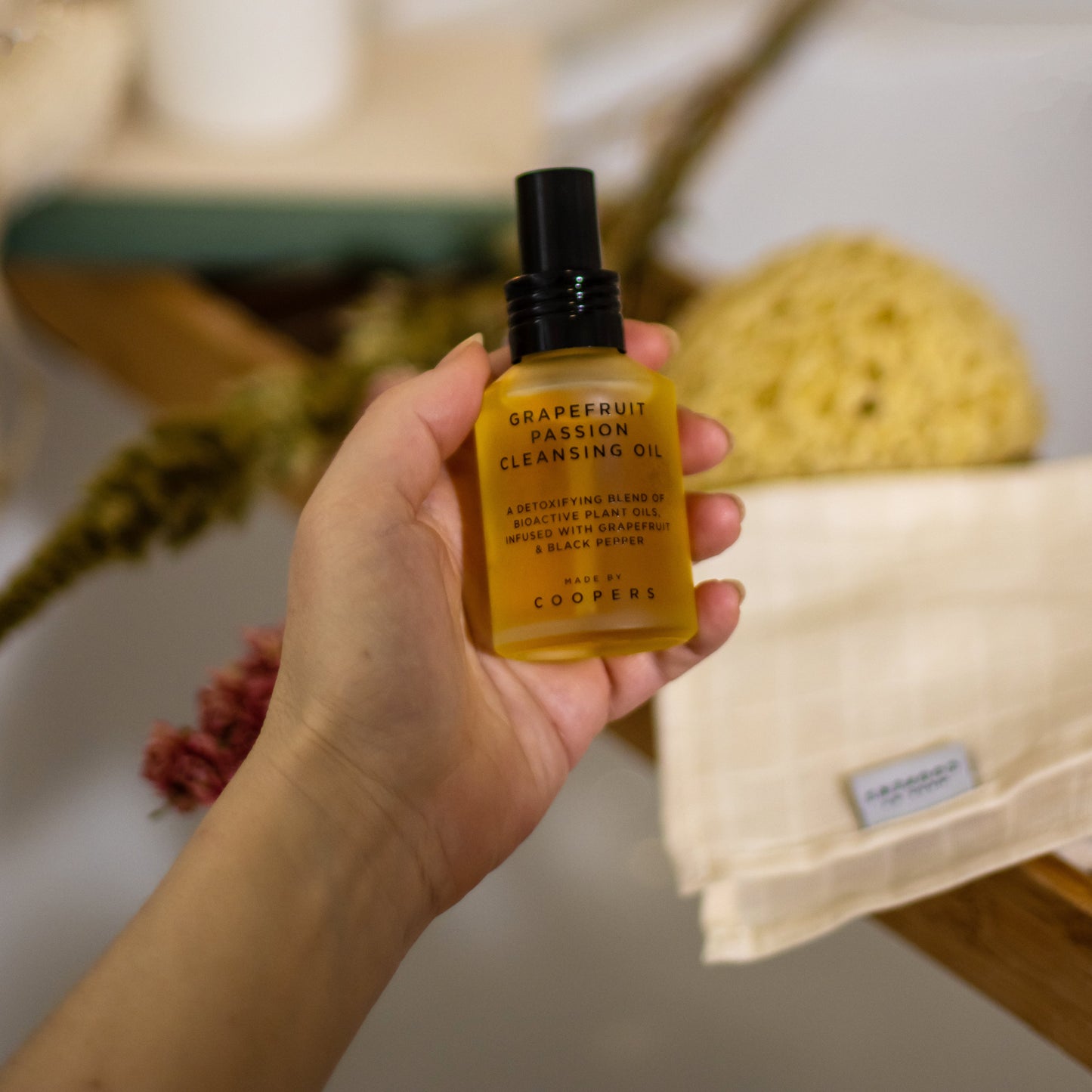 Hand holding a bottle of grapefruit passion cleansing oil with a blurred bathroom background