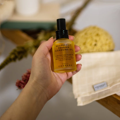 Hand holding a bottle of grapefruit passion cleansing oil with a blurred bathroom background