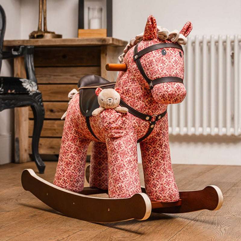 Red floral-patterned rocking horse with a teddy bear on a wooden floor.