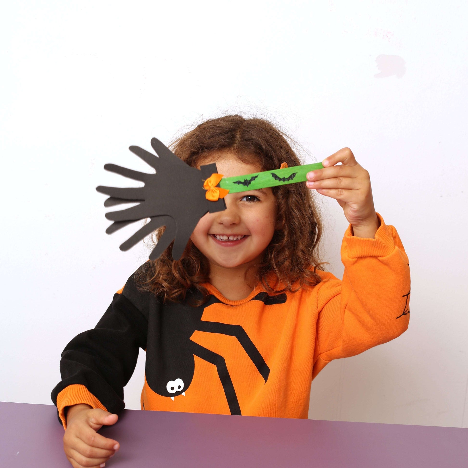 Child in Halloween costume holding a spider and a green strip with orange decorations.