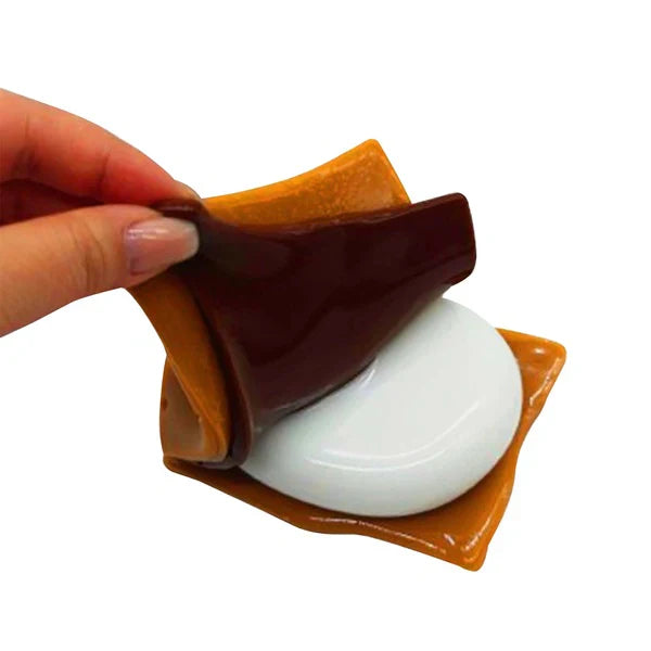 Hand holding a white spherical object with brown and orange shell-like structures on a white background