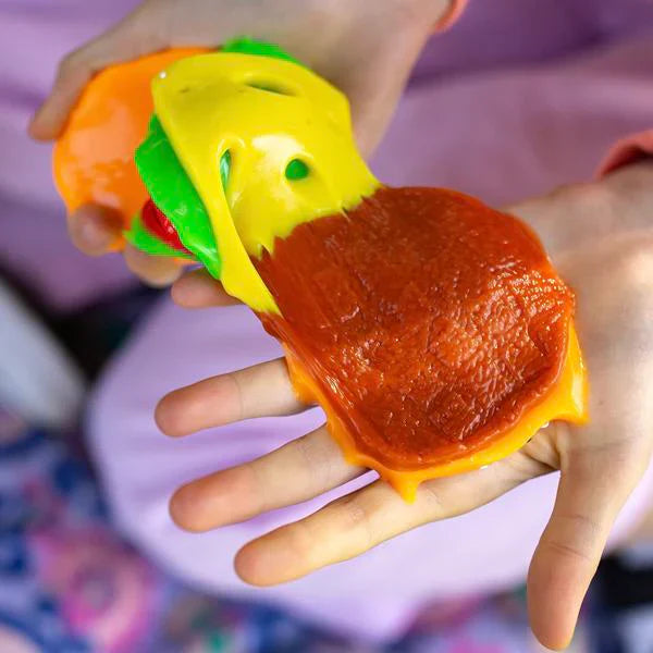 Colorful squishy toy resembling a cheeseburger held in a hand against a blurred background.