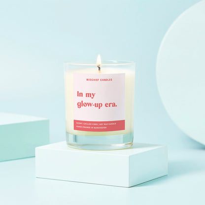 Candle with a pink label on a white platform against a light blue background