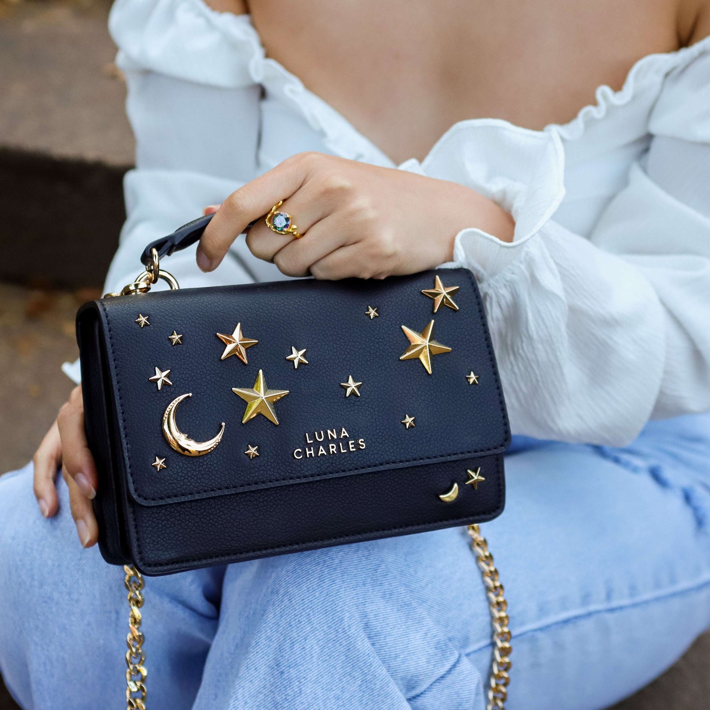 Black handbag with gold star and moon designs held by a person wearing a white top and blue jeans.