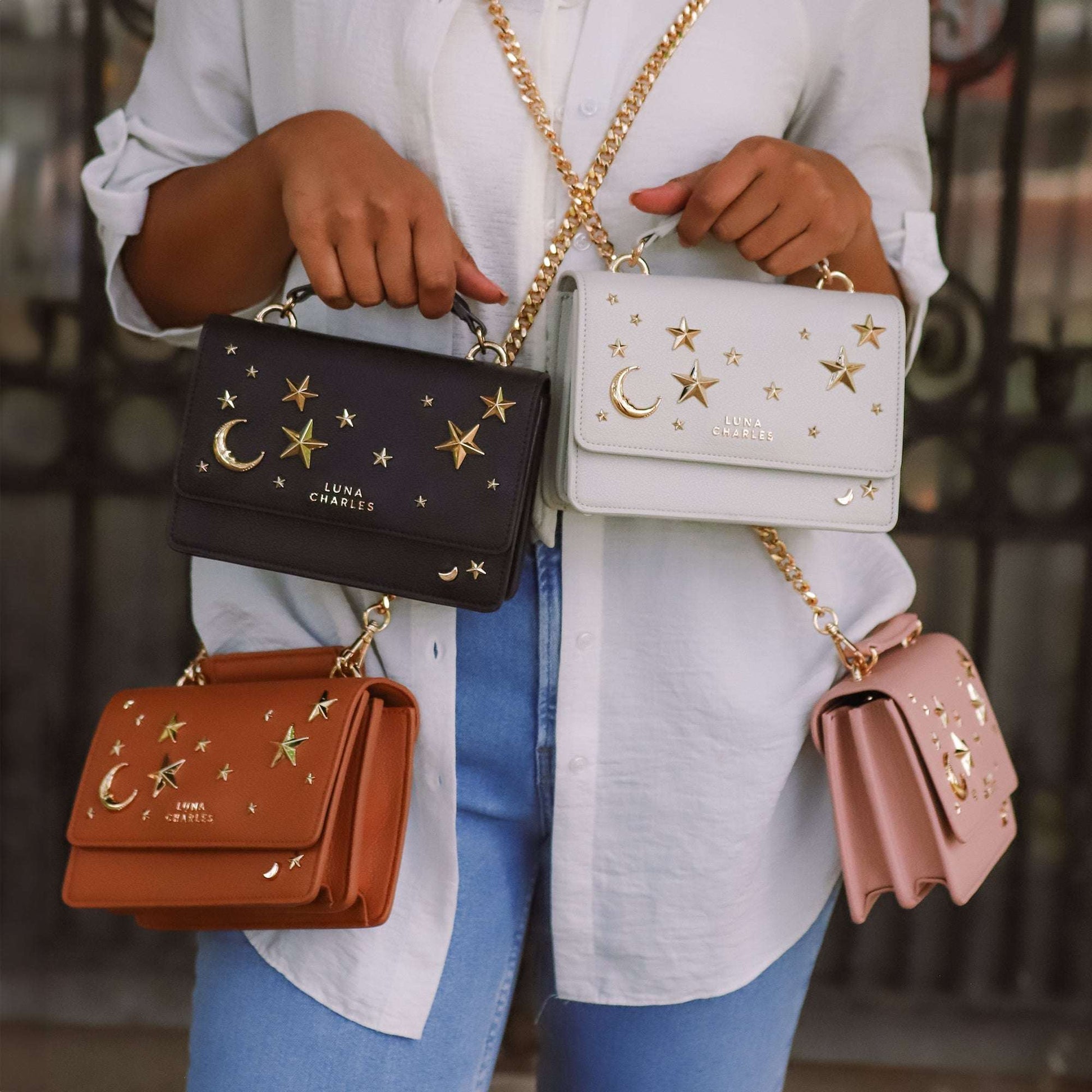 Person holding four handbags with star and moon designs, wearing a white shirt and blue jeans.