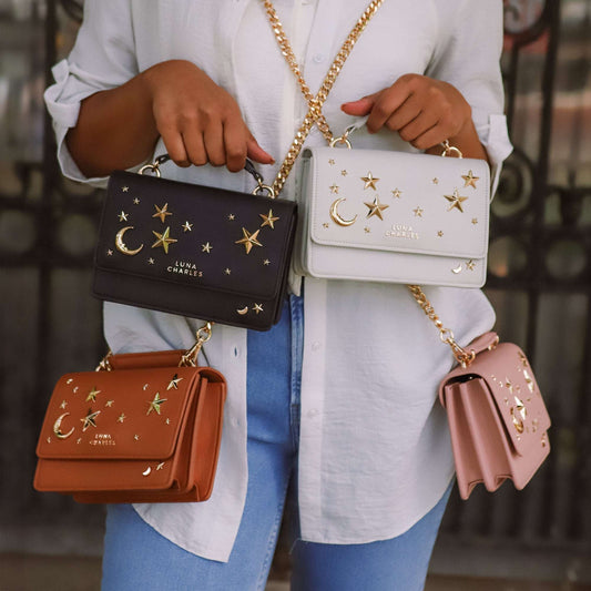 Person holding four handbags with star and moon designs, wearing a white shirt and blue jeans.