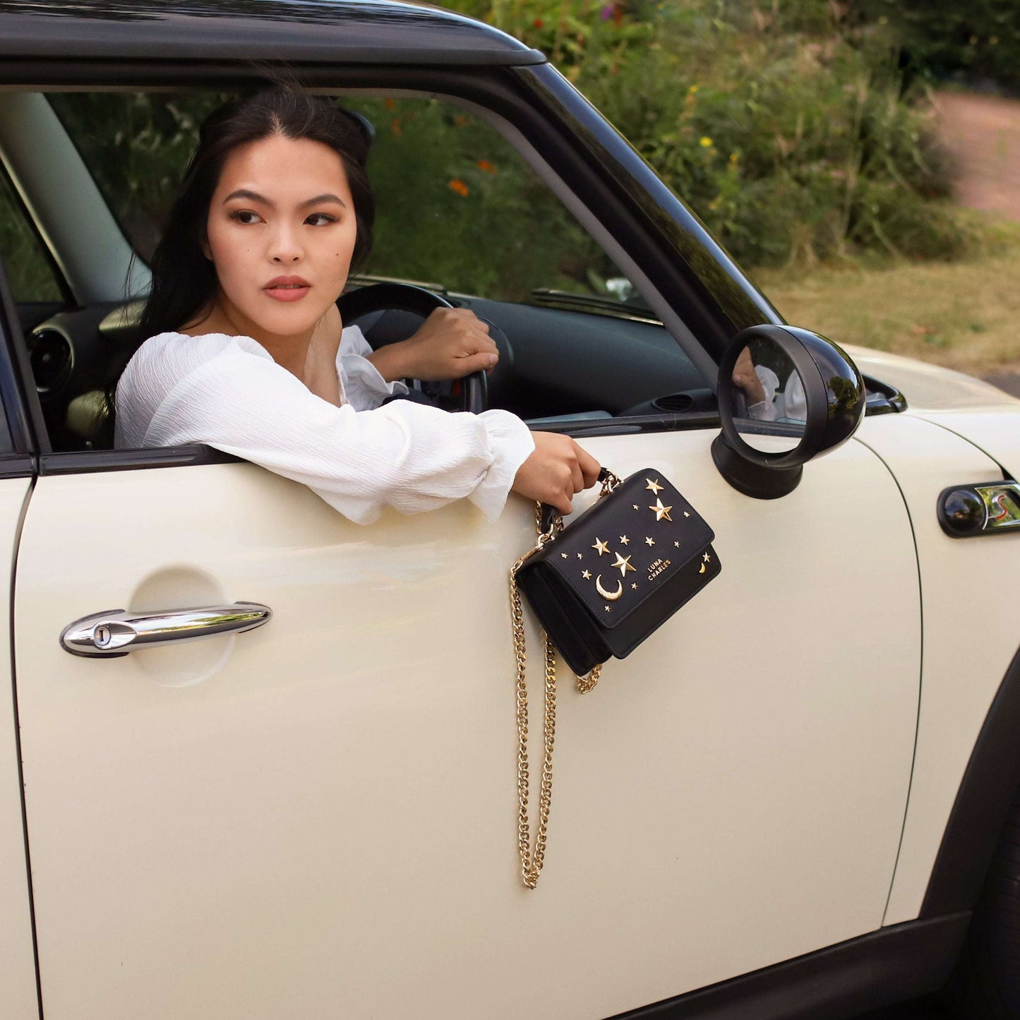 Woman sitting in a car with a black handbag featuring gold chains.