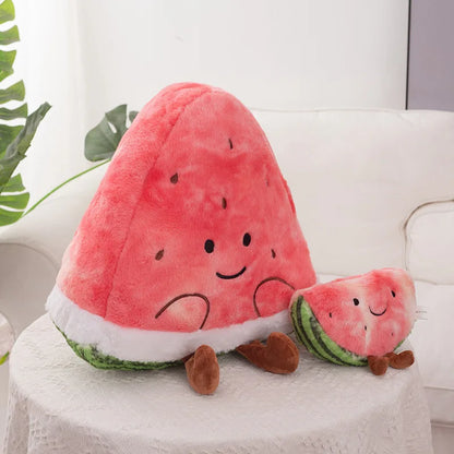 A cute plush watermelon toy with a large triangular watermelon slice and a smaller slice companion, both with embroidered smiling faces and brown feet, sitting on a white tablecloth.
