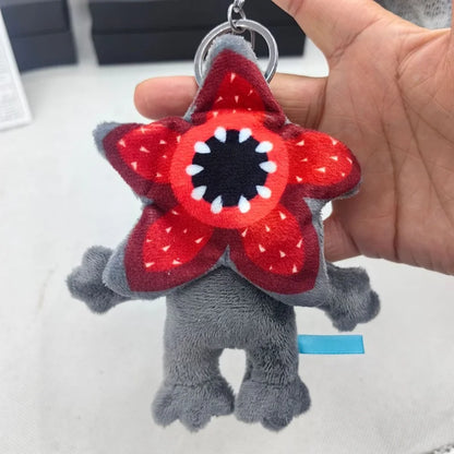 Gray plush toy with a red flower-shaped head held by a hand on a white background