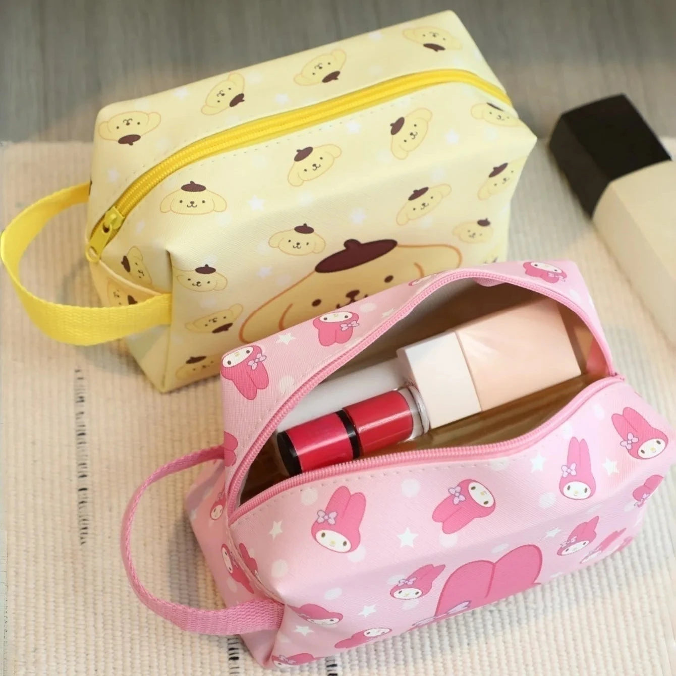 Two cosmetic bags, one yellow with bear pattern and one pink with bear pattern, on a textured surface.