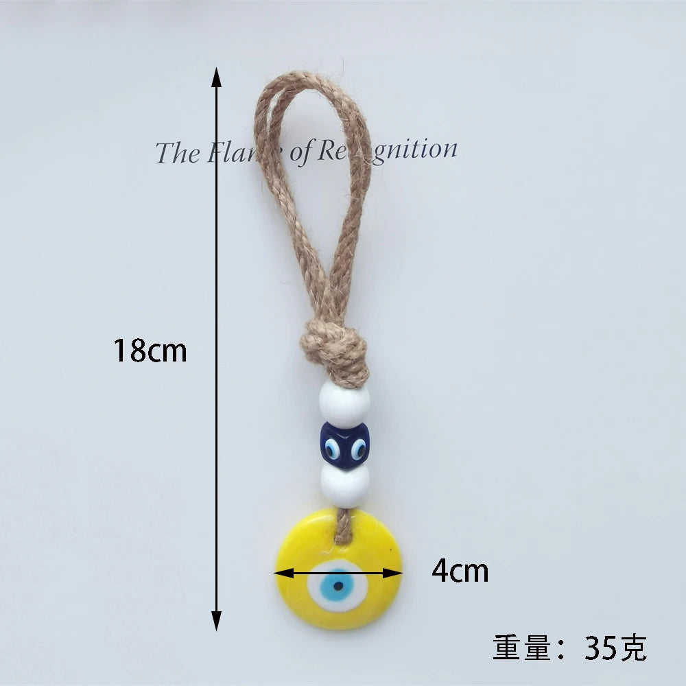 Yellow evil eye charm with a white bead and blue eye, attached to a rope, on a light gray background.