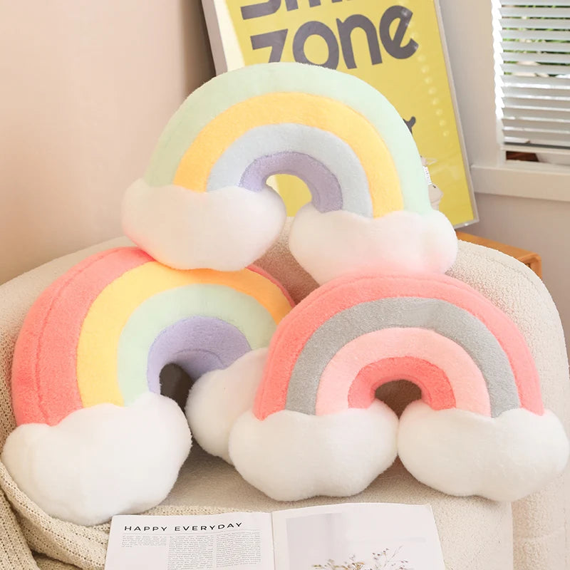 Set of rainbow-shaped cushions on a surface with a 'Happy Everyday' book in the background.
