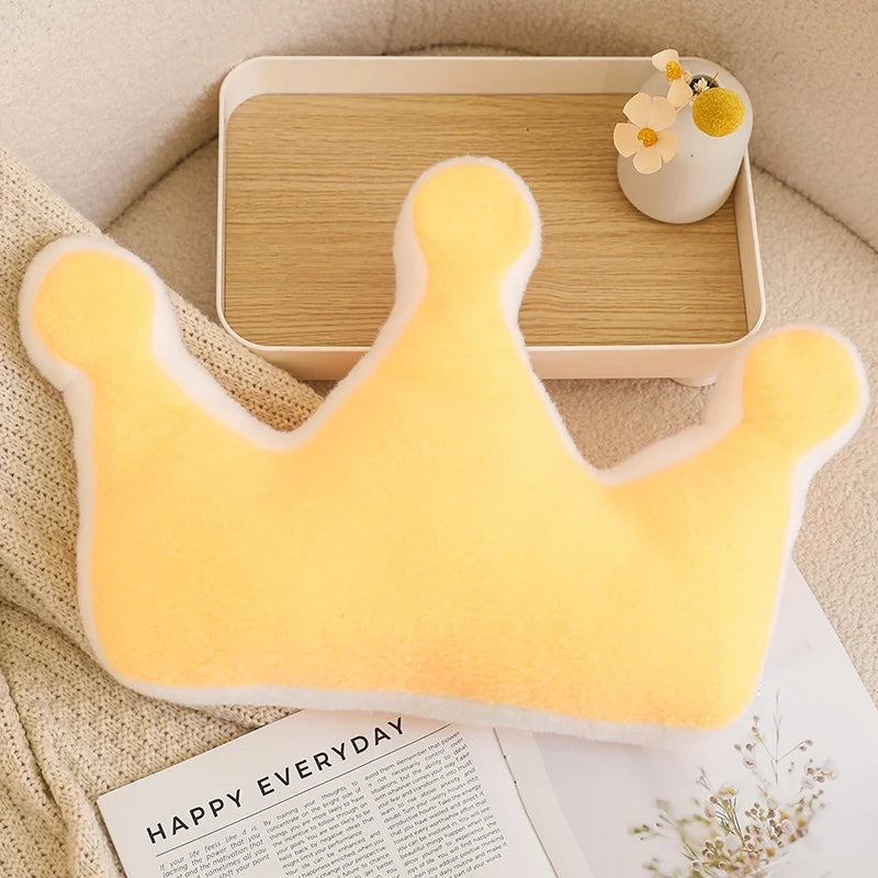 Yellow crown-shaped pillow on a surface with a tray and flowers in the background