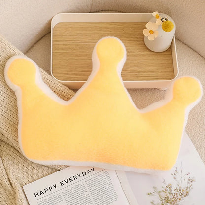 Yellow crown-shaped pillow on a surface with a tray and flowers in the background