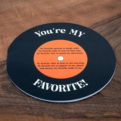 Round black coaster with orange center and white text on a wooden surface