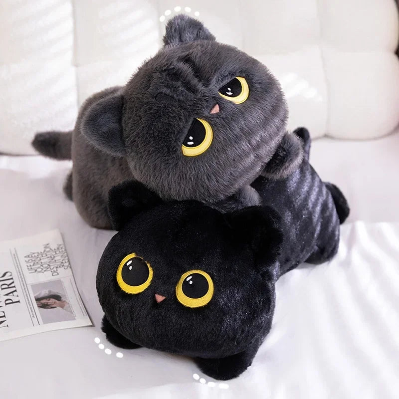 Two plush cat toys, one gray and one black, on a white surface with a magazine underneath.
