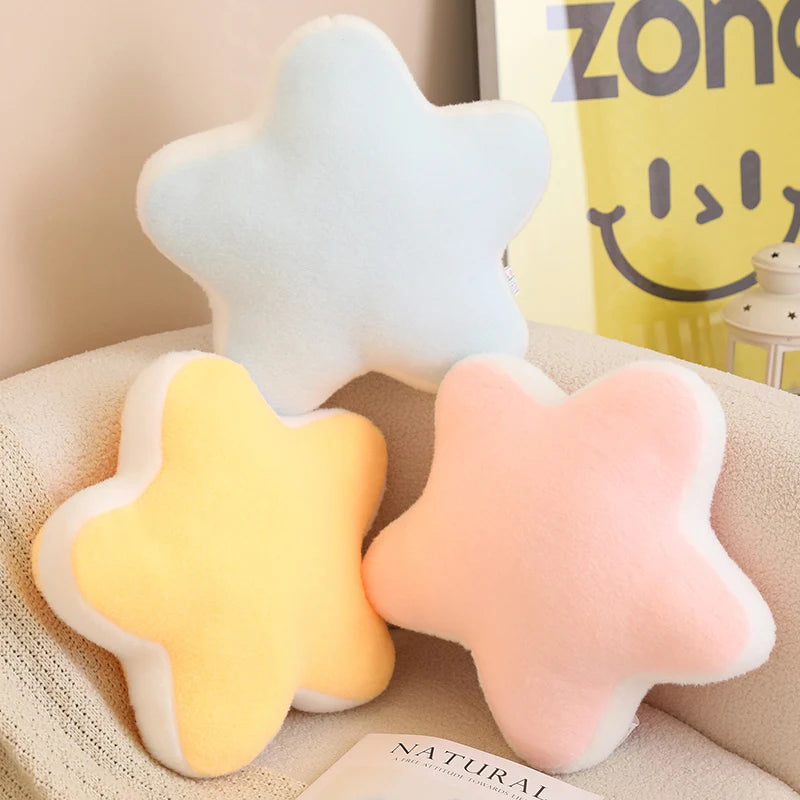 Three star-shaped cushions in white, yellow, and pink on a beige surface with a Zone 119 bag in the background.