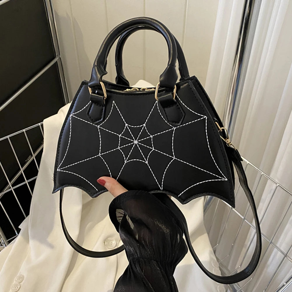 Black handbag with spider web design held by a person indoors.