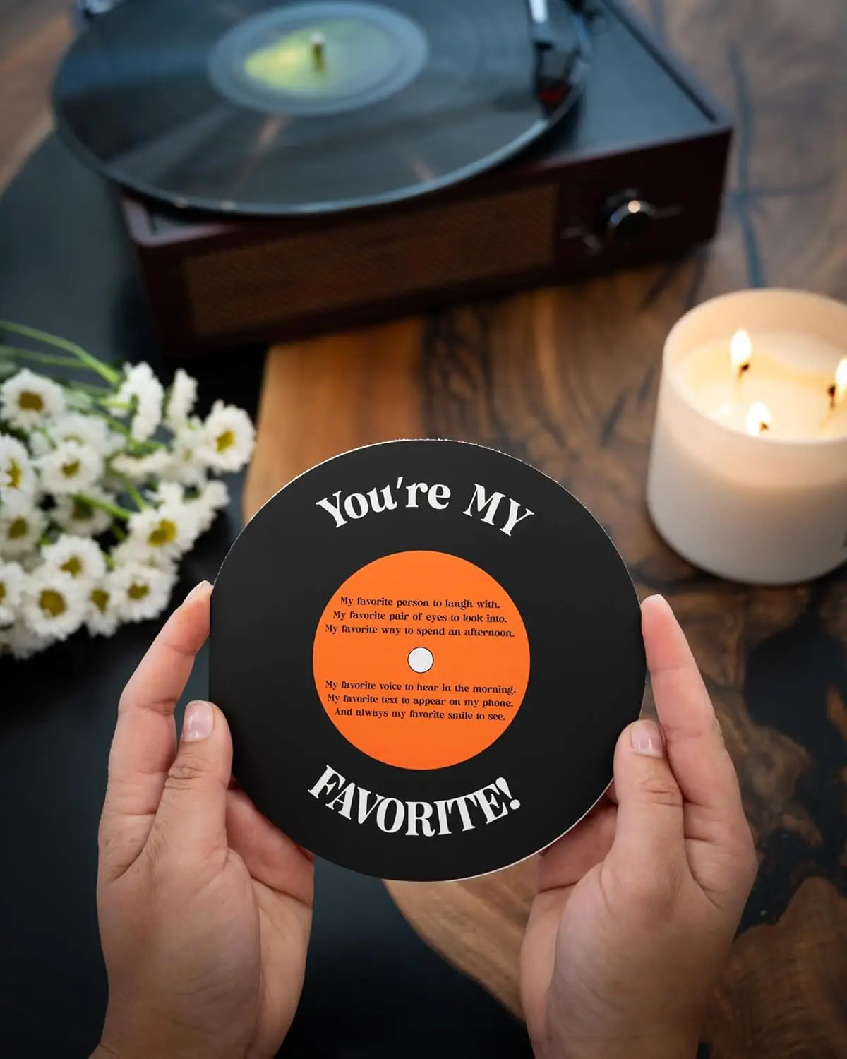 Person holding a vinyl record with 'You're MY FAVORITE!' text, with a record player and candle in the background.