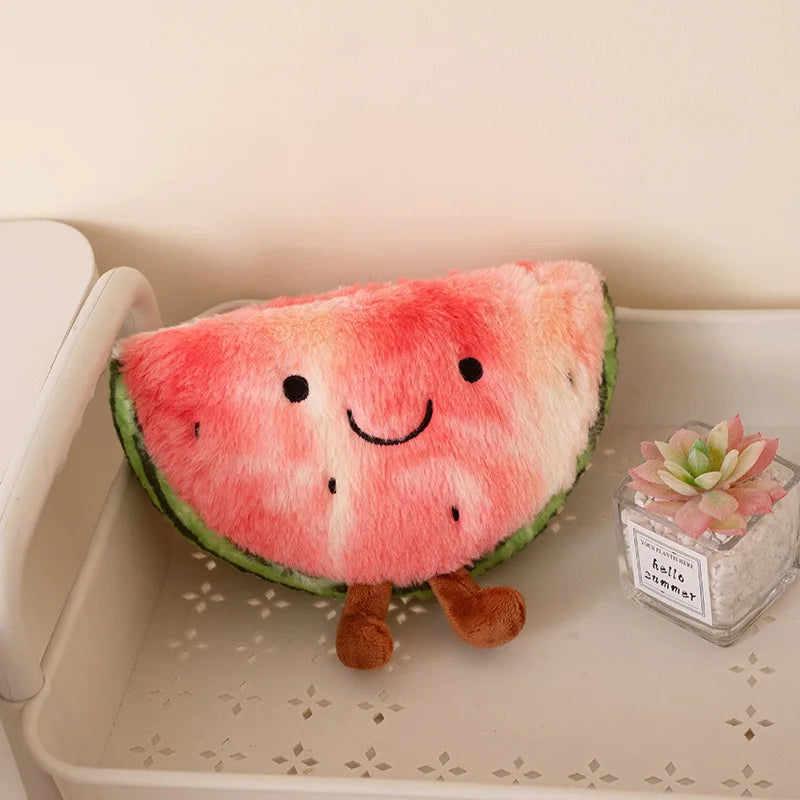 A plush watermelon slice cushion with a smiling face and small brown legs, resting on a white shelf next to a small succulent in a glass jar.