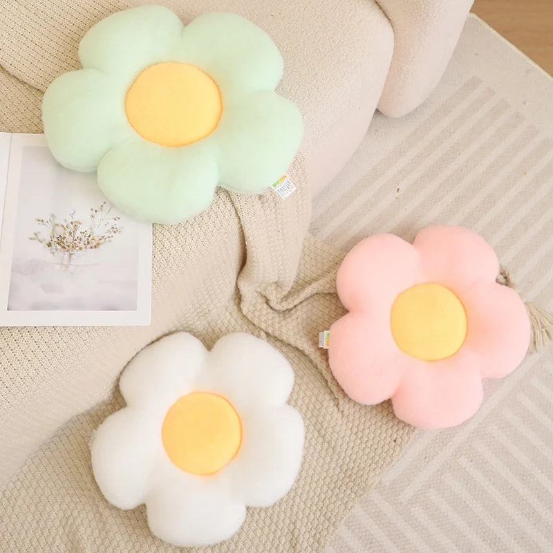 Three flower-shaped cushions in green, white, and pink on a textured surface.