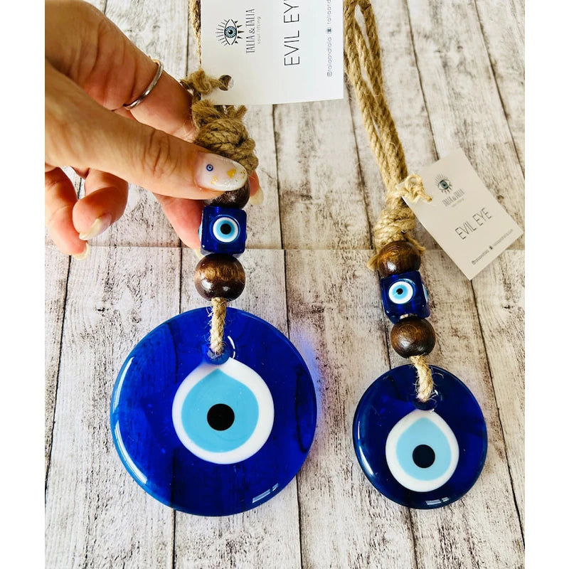 Blue evil eye pendant with wooden beads on a wooden surface, held by a hand.