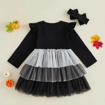 A toddler girl's Halloween costume set featuring a long-sleeve dress with a black top, white and black tiered tulle skirt, and a matching black bow headband, displayed on a beige background with decorative autumn props.