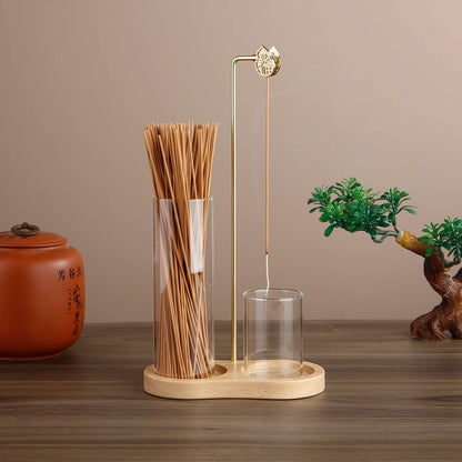A decorative incense holder with incense sticks on a wooden surface, next to a teapot and a small plant.