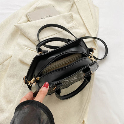 Black handbag with gold accents held by a hand against a light background