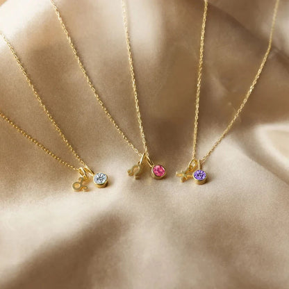 Three gold necklaces with colorful gemstones on a beige fabric background