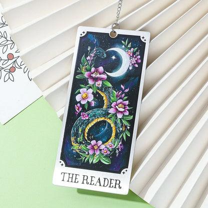 Card with 'The Reader' design featuring flowers and a moon, hanging on a white surface.