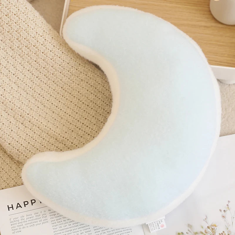 Light blue crescent moon-shaped pillow on a wooden surface with a book underneath