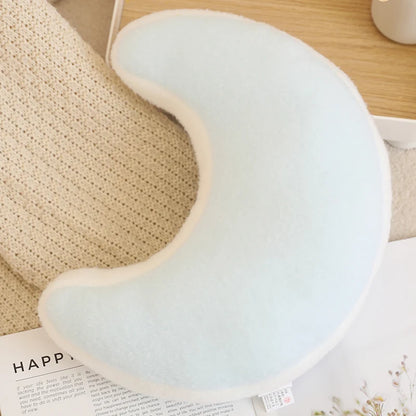 Light blue crescent moon-shaped pillow on a wooden surface with a book underneath