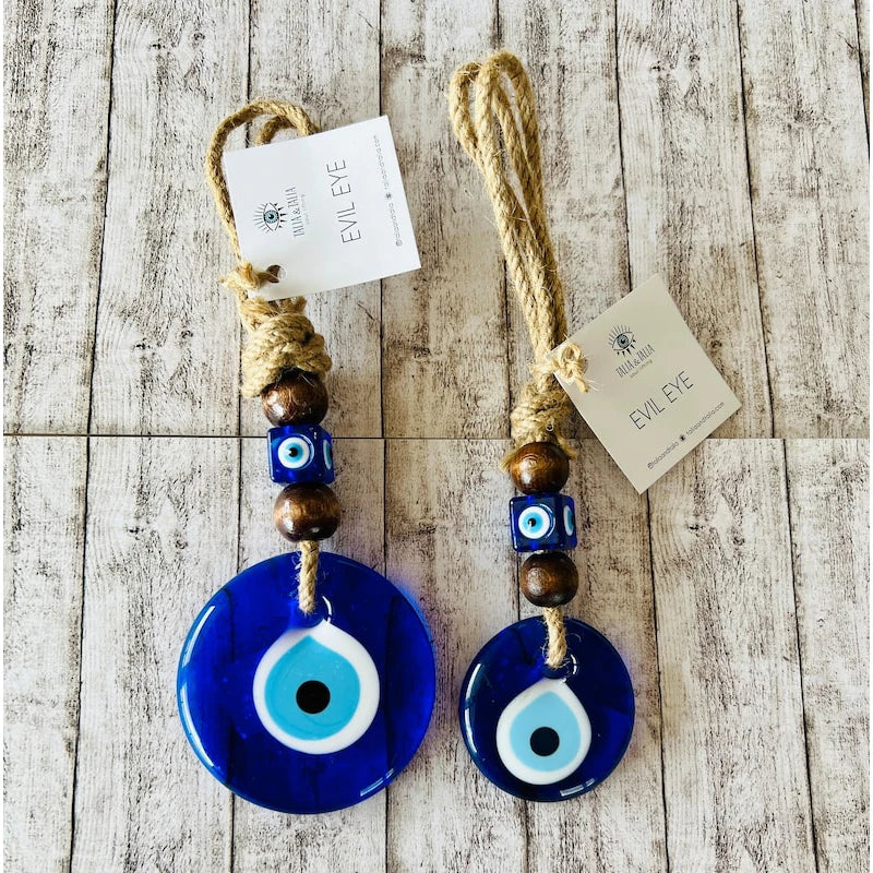 Two blue evil eye charms with wooden beads on a wooden surface, each with a tag.
