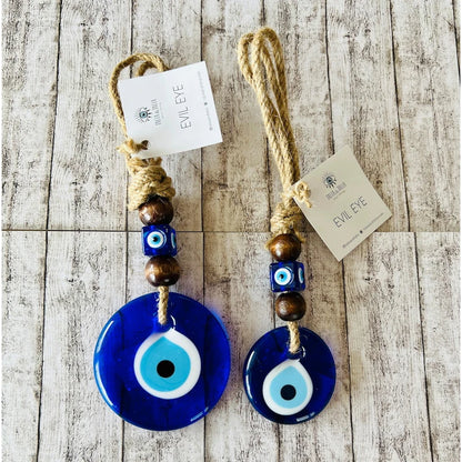 Two blue evil eye charms with wooden beads on a wooden surface, each with a tag.