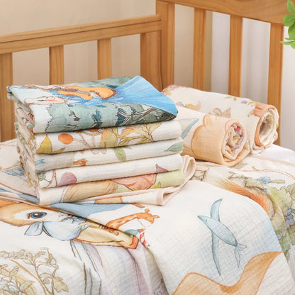 Stack of colorful quilted baby blankets with animal patterns on a wooden crib.