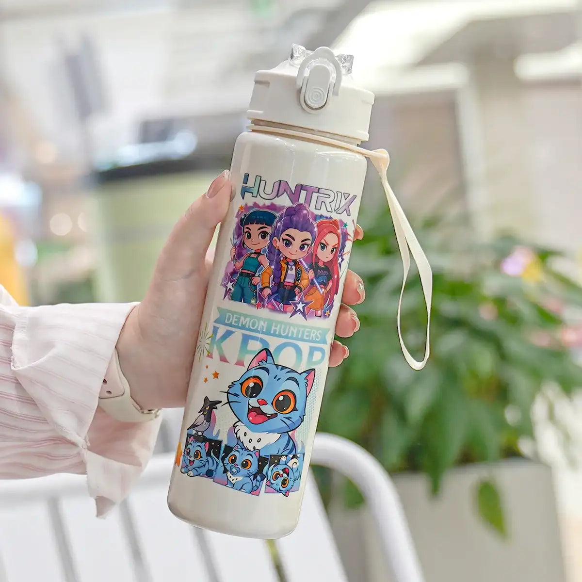 Hand holding a water bottle with cartoon characters on a blurred outdoor background