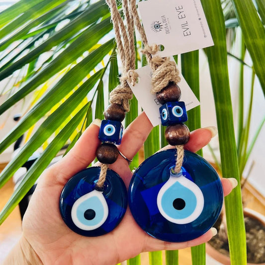 Hand holding two blue evil eye charms with a palm leaf background